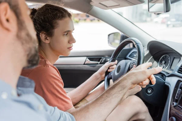 Barbudo padre apuntando a velocímetro mientras que enseñar hijo adolescente cómo conducir coche - foto de stock