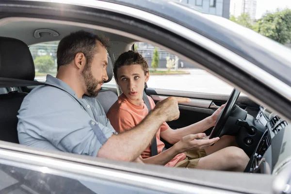 Padre barbuto parlando con figlio adolescente mentre gli insegna a guidare l'auto — Foto stock
