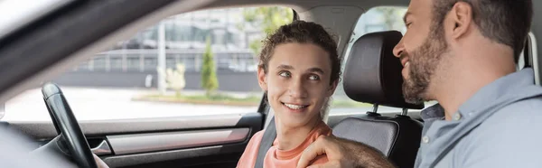 Веселий батько кладе руку на плече сина-підлітка, навчаючи його водити машину, банер — стокове фото