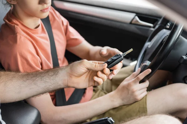 Visão cortada do pai dando a chave do carro ao filho adolescente sentado ao lado do volante — Fotografia de Stock