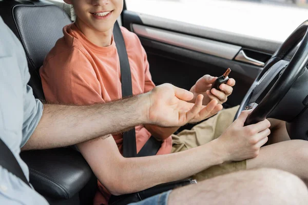 Cropped view of father giving car key to happy teenage son in modern automobile — Stock Photo