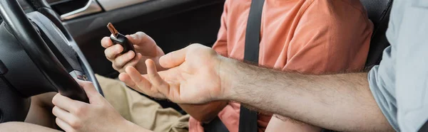 Cropped view of father giving car key to teenage son sitting next to steering wheel, banner — Stock Photo