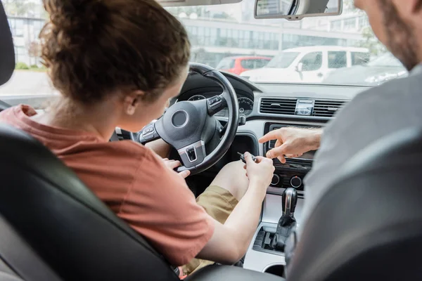Back view of father pointing with finger while showing teenage son how to start car — Stock Photo