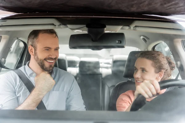Happy teenager boy holding steering wheel and looking at excited father while driving car — Stock Photo