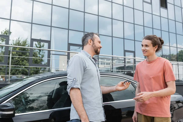 Щасливий бородатий чоловік дає ключ від автомобіля підлітковому синові біля автомобіля — стокове фото
