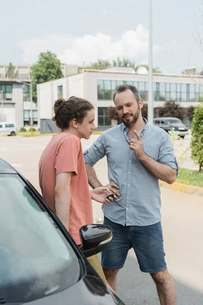 Бородатий тато попереджає сина-підлітка, стоячи разом біля машини — стокове фото