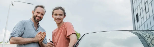 Счастливый отец и сын-подросток, стоящие рядом с современным автомобилем, баннер — стоковое фото