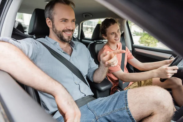 Padre barbudo feliz señalando con el dedo mientras que muestra la dirección al hijo adolescente que conduce el coche - foto de stock