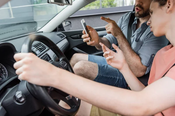 Бородатий батько вказує на смартфон, використовуючи онлайн карту, що сидить поруч з сином-підлітком в машині — стокове фото