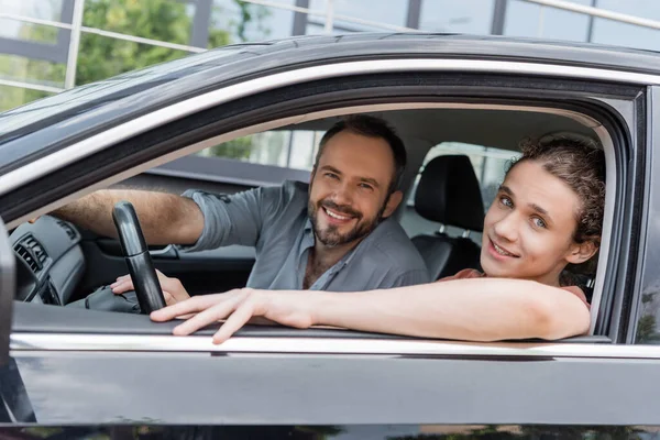 Happy dad and teenage son looking at camera while sitting together in car — Stock Photo