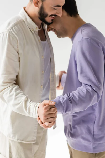 Blurred and smiling same sex couple in casual clothes holding hands during conversation with each other while standing isolated on grey — Stock Photo