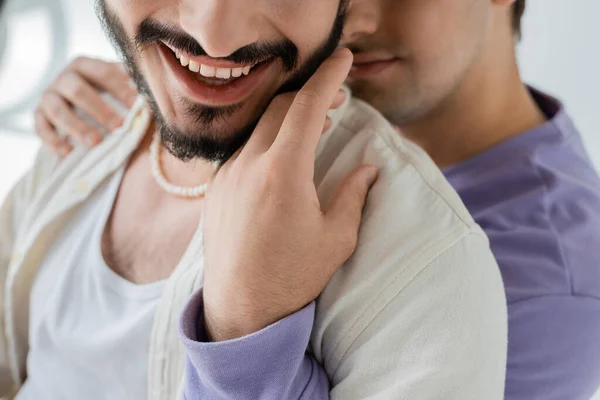 Обрезанный вид размытого гомосексуального мужчины в повседневной одежде, обнимающего и трогающего бороду беззаботного партнера в повседневной одежде на сером фоне — стоковое фото