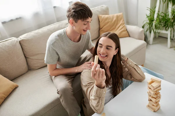High angle view of cheerful young gay couple in casual clothes playing wood blocks game on table while spending time together in living room at home — Stock Photo