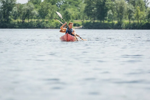 Couple d'amis sportifs multiethniques dans la vie gilets de voile en kayak avec des pagaies tout en passant week-end d'été sur la rivière sur le premier plan flou, loisirs aquatiques — Photo de stock
