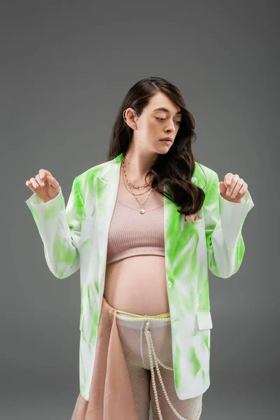 Appealing mom-to-be in crop top, trendy green and white blazer, beads belt and tights with beige chiffon cloth isolated on grey background, fashionable pregnancy concept, expectation — Stock Photo
