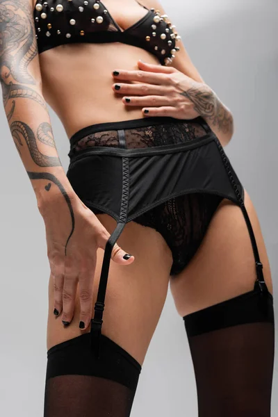 Corte vista de sexy tatuado mulher posando no sutiã com pérolas, calcinha de renda, cinto de liga e meias no fundo cinza, arte da sedução, fotografia erótica — Fotografia de Stock