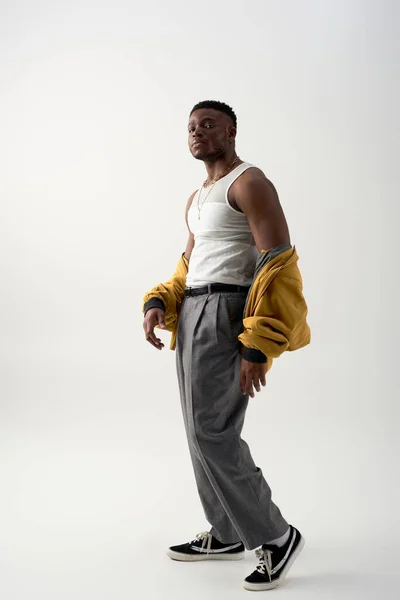 Полная длина модного молодого афроамериканца в футболке без рукавов и пиджаке бомбардировщика, стоящего на сером фоне, современная съемка со стильной одеждой, модное заявление — стоковое фото