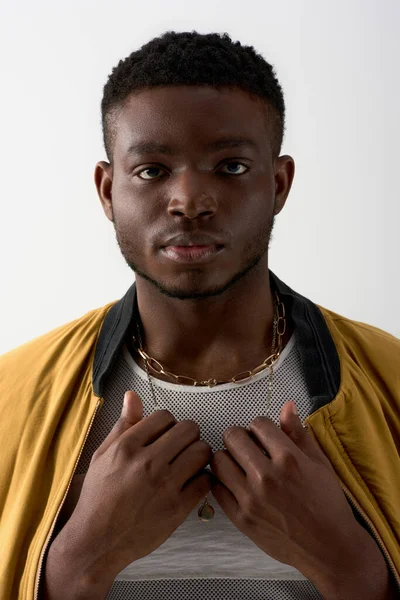 Portrait of young and trendy afroamerican model in bomber jacket and golden necklaces looking at camera isolated on grey, contemporary shoot featuring stylish attire, fashion statement — Stock Photo