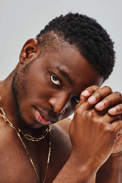 Portrait of good looking and shirtless afroamerican man with trendy hairstyle and golden necklaces looking at camera isolated on grey, confident and modern pose, fashion shoot — Stock Photo