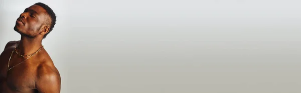 Uomo afroamericano rilassato e senza camicia con collane dorate che chiudono gli occhi e in piedi isolato su posa grigia, sicura e moderna, servizio fotografico, banner — Foto stock