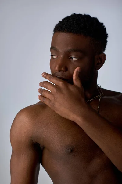 Jeune homme afro-américain torse nu et beau avec des colliers dorés regardant loin isolé sur la pose grise, confiante et moderne, tournage de mode — Photo de stock