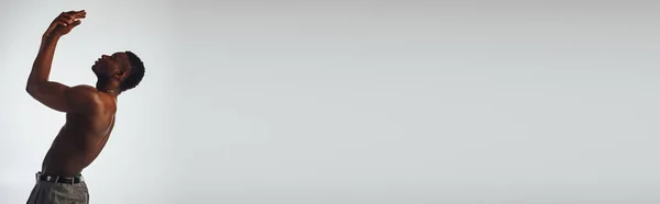 Vista lateral do modelo afroamericano muscular e sem camisa em calças isoladas em pose cinza, confiante e moderna, sessão de moda, banner, homem sem camisa — Fotografia de Stock