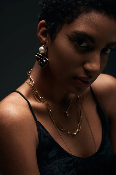 Retrato de modelo afroamericano de moda con maquillaje de noche y accesorios dorados mirando a la cámara aislada en negro con iluminación, alta moda y aspecto de noche - foto de stock