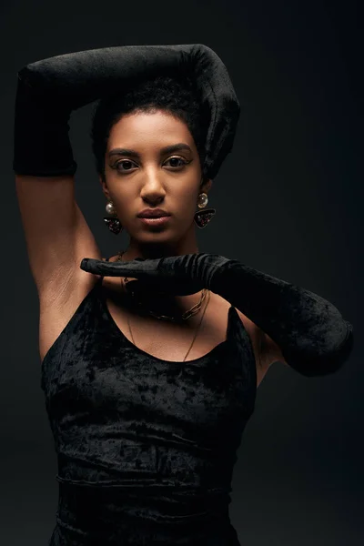 Портрет елегантної афроамериканської моделі в вечірній сукні, золоті аксесуари і рукавички позують і дивляться на камеру, стоячи ізольовано на чорному, високій моді і вечірньому погляді — стокове фото