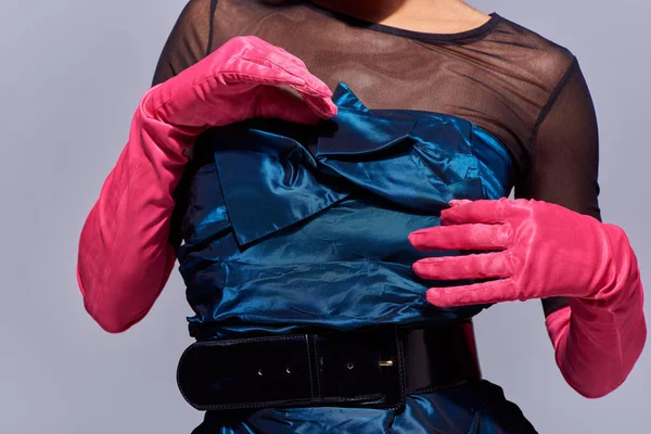 Обрізаний вид молодої моделі в стильній коктейльній сукні та рожевих рукавичках, що торкаються лука, стоячи ізольовано на сірому, сучасному поколінні концепції моди z, деталі, пояс, жіночий — стокове фото