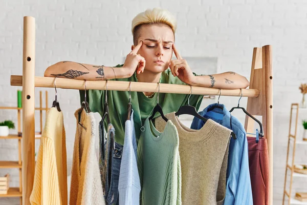 Wardrobe items sorting, conscious decluttering, pensive tattooed woman touching head while thinking near rack with casual clothes at home, sustainable fashion and mindful consumerism concept — Stock Photo