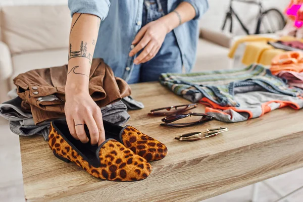 Vista cortada de mulher tatuada colocando sapatos de impressão animal na mesa com itens em segunda mão e óculos de sol, consumo ético, troca, vida sustentável e conceito de consumismo consciente — Fotografia de Stock