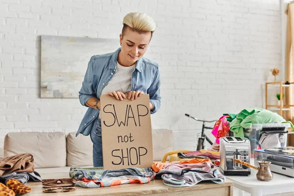 Mindful consumerism, pleased tattooed woman smiling next to swap not shop card, second-hand items, electric toaster, vinyl record player and cezve, sustainable living and circular economy concept — Stock Photo