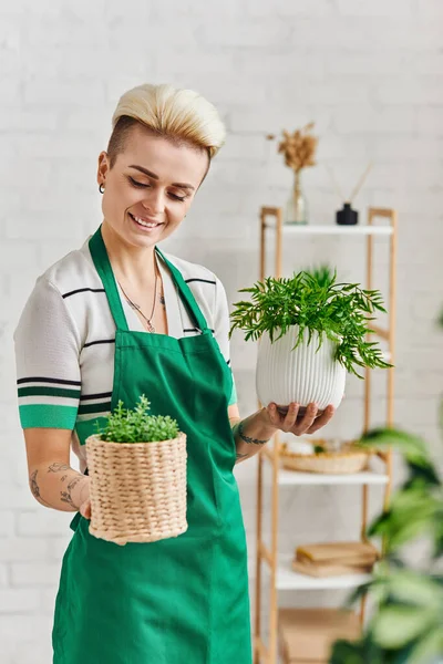 Plant lover, eco-conscious lifestyle, pleased tattooed woman with radiant smile holding flowerpots with green plants in modern apartment, sustainable home decor and green living concept — Stock Photo