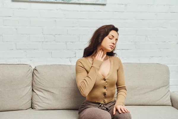 Junge brünette Frau bei einer Lymphsystem-Massage zur Drainage, während sie auf der Couch im Wohnzimmer in einem modernen Haus sitzt, Selbstversorgungsritual und ganzheitliches Wellness-Praxiskonzept, Spannungsabbau — Stockfoto