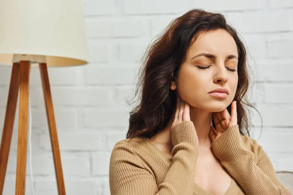 Young brunette woman closing eyes during self-massage of lymphatic system and thyroid gland function support at home, self-care ritual and holistic wellness practices concept, tension relief — Stock Photo