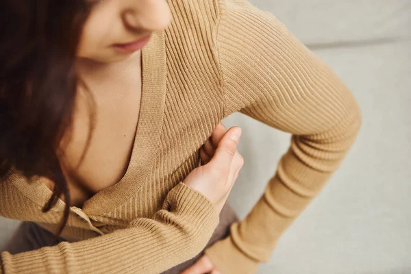 Верхний вид юной брюнетки в коричневом свитере, массирующей лимфатические узлы подмышки во время дренажного массажа на диване дома, повышение самосознания и расслабления тела, балансирование энергии — стоковое фото