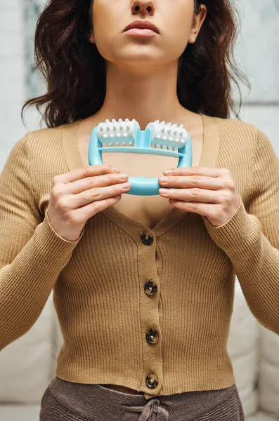 Cropped view of young woman in casual brown jumper holding handled massager for self-massage at home at background, enhancing self-awareness and body relaxation concept, balancing energy — Stock Photo