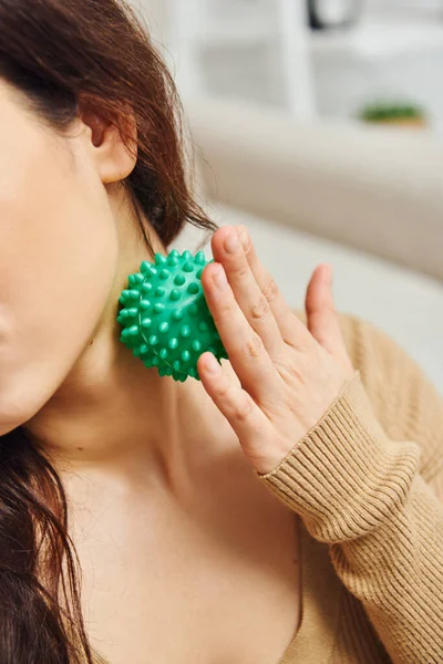 Cropped view of young woman in brown jumper massaging lymphatic nodes with manual massage ball for drainage at home, lymphatic system support and home-based massage, tension relief — Stock Photo