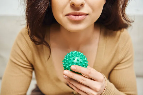 Cropped view of young brunette woman in blurred jumper holding manual massage ball in blurred house, body relaxation and holistic wellness practices, balancing energy concept — Stock Photo