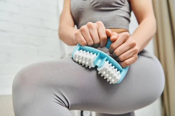 Close up view of young blurred woman in sportswear massaging leg with handled massager while standing at home, home-based massage and holistic practices concept, myofascial release — Stock Photo