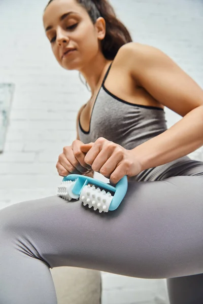 Low angle view of young blurred woman in activewear massaging leg with handled massager in living room at home, home-based massage and holistic practices concept, myofascial release — Stock Photo