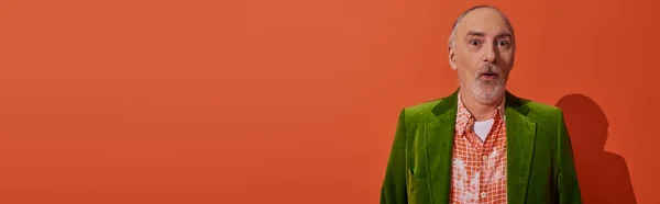 Trendiger älterer Herr mit schockiertem Gesichtsausdruck, der auf rot-orangefarbenem Hintergrund in die Kamera blickt, graues Haar und Bart, grüner Velours-Blazer, Mode- und Alterskonzept, Banner mit Kopierraum — Stockfoto