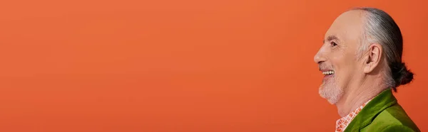 Profil des fröhlichen älteren Mannes mit grauen Haaren und Bart, der auf leuchtend orangefarbenem Hintergrund lächelt, persönlicher Stil, grüner Velours-Blazer, positives und optimistisches Altern, Banner mit Kopierraum — Stockfoto