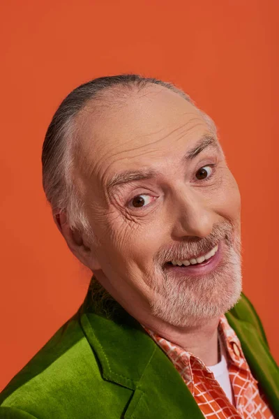 Felicidad y optimismo, retrato de hombre mayor guapo con sonrisa radiante, pelo gris y barba arreglada mirando a la cámara sobre un fondo naranja vibrante, concepto de envejecimiento positivo y de moda - foto de stock