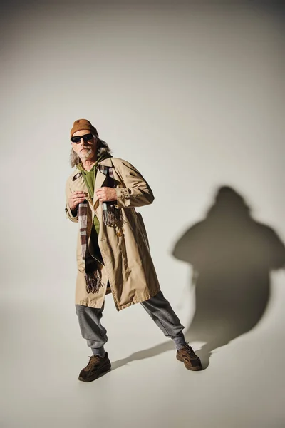 Ausdrucksstarke und modische Persönlichkeit, vollwertiger älterer Mann in Hipster-Kleidung und dunkler Sonnenbrille posiert auf grauem Hintergrund mit Schatten, positives Lifestylekonzept — Stockfoto