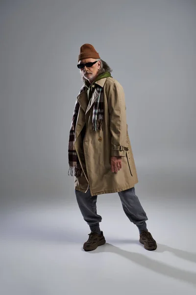 Volle Länge des Senior-Hipster-Mannes mit dunkler Sonnenbrille und modischer Freizeitkleidung, der auf grauem Hintergrund vor der Kamera steht, ausdrucksstarke Persönlichkeit, stilvolles Alterskonzept — Stockfoto