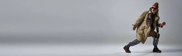 Senior Model im Hipster-Stil in dunkler Sonnenbrille und modischer Freizeitkleidung, die wegschaut und auf grauem Hintergrund posiert, Banner mit Kopierplatz — Stockfoto