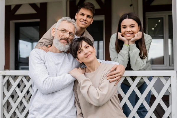 Family photo, happy parents day, middle aged parents hugging near teenage daughter and young adult son on porch of summer house, family celebration, bonding, moments to remember, modern parenting — Stock Photo