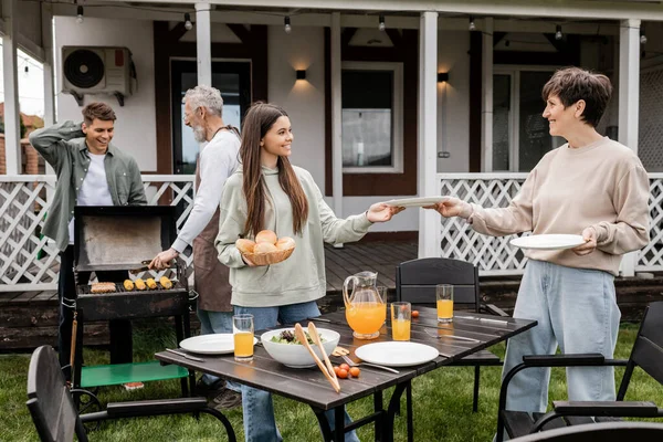 Parents day, happy teenage girl helping mother serving the table, father and son making bbq, grilling corn, backyard of summer house, suburban life, family bbq party, celebration — Stock Photo
