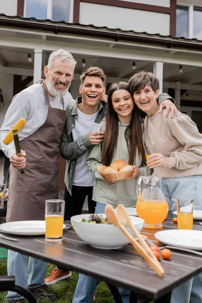 Parents day, family photo, happy middle aged parents having bbq party with young adult son and teenage daughter, father holding tongs with grilled corn, summer house, suburban life — Stock Photo